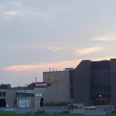 A large building stands in the middle of a parking lot at dusk.