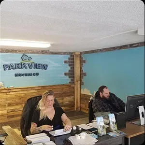 Two people working in an office with rustic decor and a sign labeled "Parkview Movers Co." are capturing images for their company's portfolio.