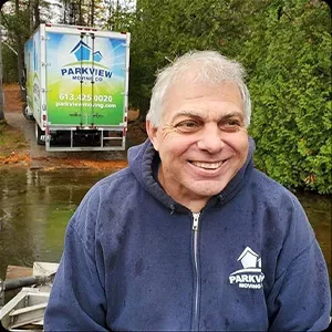 An image of a smiling man wearing a jacket branded with "parkview moving" in front of a moving truck with the same company name.