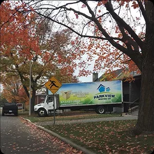 A truck with an advertisement on its side, captured in a photography session, parked beneath autumn trees with fallen leaves on the ground.
