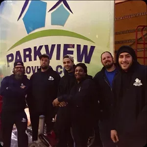 Group of six individuals posing for a photo gallery in front of a sign that reads "Parkview Moving Co.