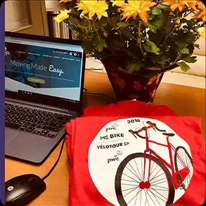 A laptop displaying "moving made easy" next to a red t-shirt with a bike print and a potted plant with yellow flowers, all arranged for a photography session.
