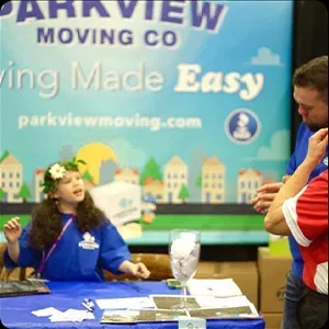 A person in a blue jacket speaking with a visitor at a promotional booth for a moving company, surrounded by images.