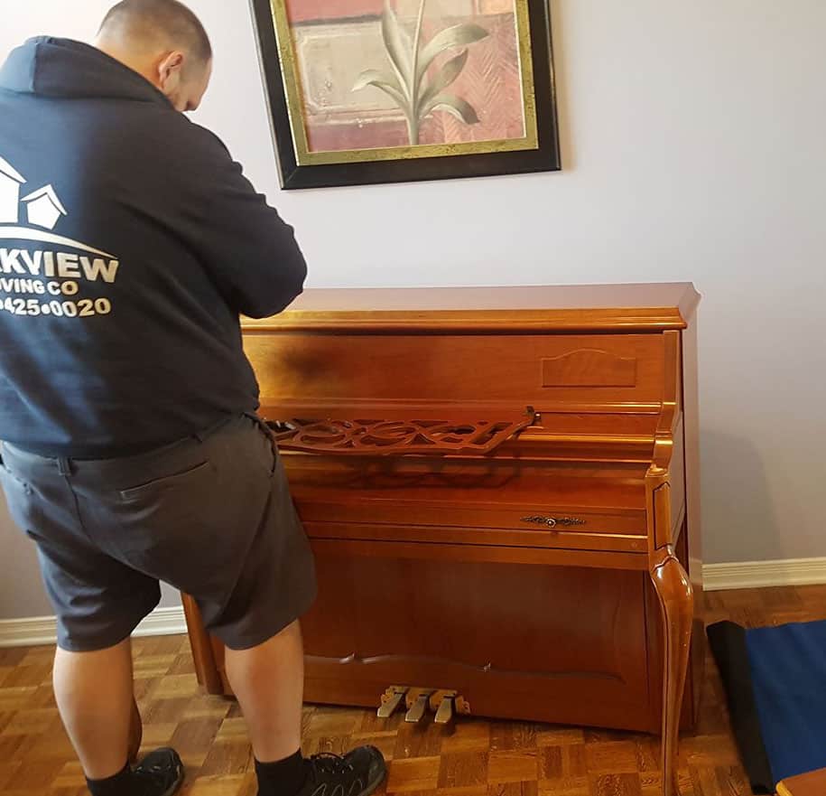Mover standing beside a wooden piano, preparing it for transport.