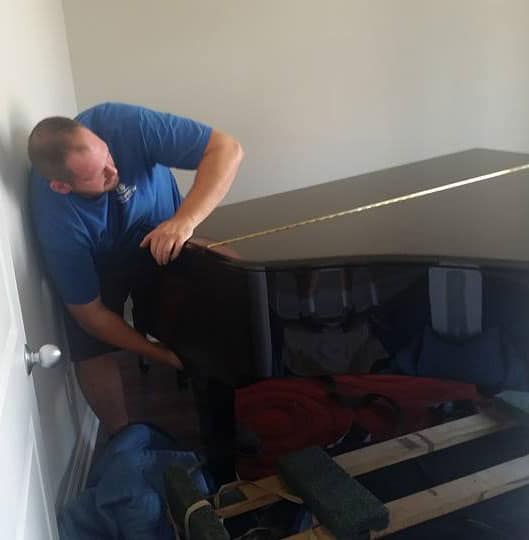 Mover transporting a black grand piano into a room with furniture pads on the floor, demonstrating the expertise of Ottawa piano movers.