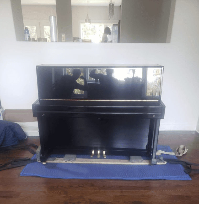 Black upright piano standing on a blue protective mat.