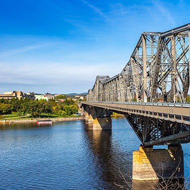 Steel truss bridge over a wide river in Gatineau, framed by trees and buildings under a clear sky—a view admired by local movers.