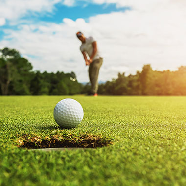 Golf ball near the hole on a sunny Kanata course, with a golfer preparing to putt.